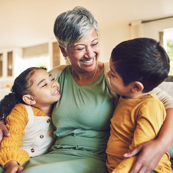 An elderly woman holding two children and smiling.
