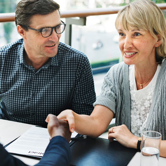 An older man and woman sitting in a meeting with a financial rep.
