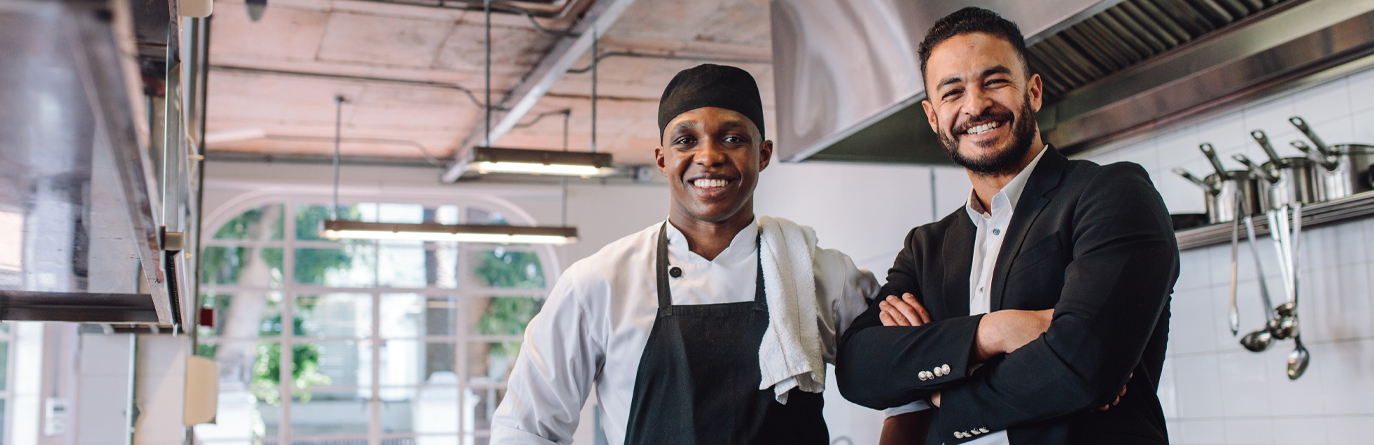 Two men standing together and smiling in a kitchen.